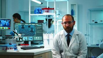 Tired doctor looking exhausted at camera in modern equipped lab late at night. Medical chemist team examining virus evolution using high tech and chemistry tools for research, vaccine development. photo
