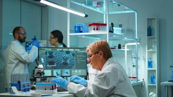 Microchemist doing research at night checking blood liquid in test tube typing results on pc in modern equipped lab. Examining virus evolution using high tech for vaccine development against covid19 photo