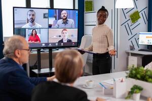 Black manager woman talking with remotely colleagues on call at tv screen, presenting new business partners. Business people talking to webcam, do online conference participate internet brainstorming, distance office discussion. photo