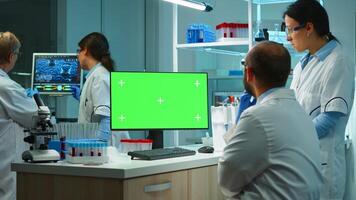 Team of microbiologists researching using computer with green screen overtime sitting in modern equipped lab. Doctors doing vaccine research writing on device with chroma key, isolated, mockup display photo