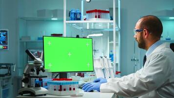 Doctor working at computer with green screen over time sitting in modern equipped lab. Team of microbiologists doing vaccine research writing on device with chroma key, isolated, mockup display. photo