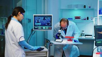 Scientist researcher using microscope in laboratory while nurse taking notes on computer working overtime. Medical healthcare technology and pharmaceutical research and development concept. photo