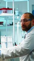 Worn out doctor typing on computer and looking exhausted at camera in equipped lab late at night. Medical chemists examining virus evolution using high tech for scientific research, vaccine development. photo