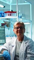 Portrait of senior scientist woman looking exhausted at camera sitting in equipped lab late at night. Team examining virus evolution using high tech for scientific research, vaccine development photo