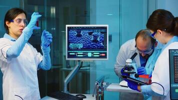 Senior chemist analysing blood sample while coworkers discussing in background about vaccine development working overtime in chemistry equipped laboratory. photo