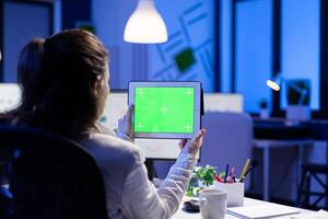 Manager woman holding tablet with green screen monitor during online web conference. Entrepreneur looking at desktop monitor display with green mockup, chroma key sitting at desk in business office photo