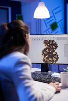 Focused architect working at new project using computer doing gear prototype late at night sitting at desk in start-up office. Industrial woman engineer studying on pc for development cad software photo