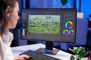 Focused editor retoucher editing color grade on professional computer sitting at desk in creative office at midnight. Freelancer editor start up new movie project processing audio film montage. photo