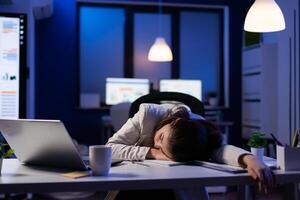 Exhausted overload business woman falling asleep on desk with open laptop while working on marketing project in start up company office. Entrepreneur using modern technology network late at night photo