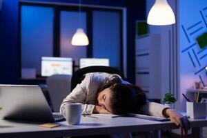 Entrepreneur working overtime on marketing project, falling asleep on desk while looking at financial documents trying to respect the deadline. Employee using modern technology network wireless photo