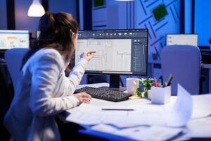 Over the shoulder shot of engineer woman drawing architectural plans and looking at cad software on desktop computer. Designer using arhitecture blueprints of buildings creating industrial prototype photo