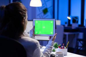 Manager woman holding tablet with green screen monitor during online web conference. Entrepreneur looking at desktop monitor display with green mockup, chroma key sitting at desk in business office photo