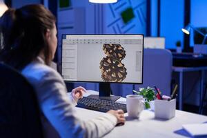 Focused architect working at new project using computer doing gear prototype late at night sitting at desk in start-up office. Industrial woman engineer studying on pc for development cad software photo