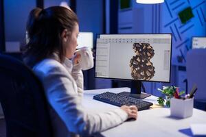 Focused architect working at new project using computer doing gear prototype late at night sitting at desk in start-up office. Industrial woman engineer studying on pc for development cad software photo