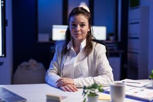 Exhausted businesswoman looking tired in camera sighing resting head in palm late at night in business office. Focused entrepreneur using technology network wireless, working at marketing statistics photo
