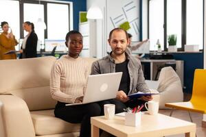 POV of diverse colleagues discussing about financial strategy during meeting using webcam sitting on couch in start up office, working for new business. Multiethnic coworkers analysing reports. photo
