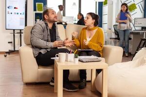 Business colleagues arguing, yealing each other during work hours sitting on the couch, while diverse colleagues working scared in background. Coworkers having conflict because of mistakes from project photo
