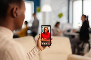 Over the sholder of black employee discussing with partner on call using phone in start up business office. Black woman during meeting, online conferencel planning new financial project photo