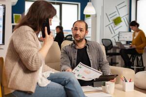 Executive business woman having a professional financial call on smartphone. Colleagues consulting talking statistics charts on clipboard in company modern office. photo