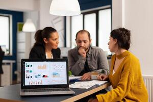Laptop screen ready for financial project presentation placed on desk while business people work in background. Diverse employees gathered in co-working, working process in busy company, teamwork help photo