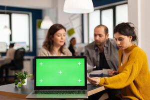 Laptop with green screen chroma key display. mock up desktop ready for presentation placed on desk while business people work in background. Group of employees using notebook with isolated monitor photo