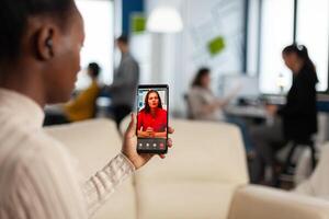 Over the sholder of black employee discussing with partner on call using phone in start up business office. Black woman during meeting, online conferencel planning new financial project photo