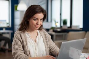 Satisfied manager checking financial statistics and graphs typing on laptop sitting at desk working in business start up company. Diverse team analyzes statistics data in modern office photo