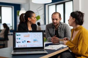 Business woman talking about financial project, taking notes, discussing start up ideas using laptop. Diverse employees gathered in co-working, working process in busy company, teamwork help concept photo