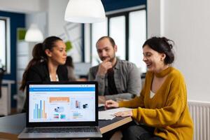 Business woman talking about financial project, taking notes, discussing start up ideas using laptop. Diverse employees gathered in co-working, working process in busy company, teamwork help concept photo