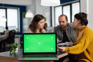 Businesspeople analysing annual financial reports sitting at desk in back of laptop with green screen chroma key display, mock up desktop. Leader explainig project strategy using greenscreen pc photo
