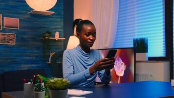 Black businesswoman browsing using smartphone sitting in living room office taking a break after hard work. African remote employee working overtime respecting deadline chatting with team. photo