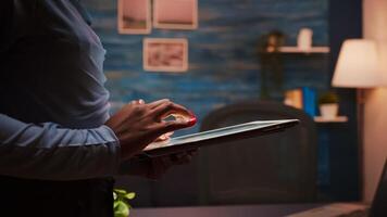 Close up of african employee texting, sending and reading messages during her break standing in living room late at night. Focused black employee using modern technology network wireless overworking photo