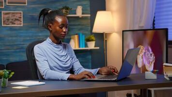 Tired black businesswoman working overtime reading projects sitting at desk in living room using laptop. Busy focused employee using modern technology network wireless overworking for job searching photo
