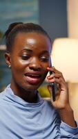 Remote black employee speaking at phone while working at laptop late at night. Busy focused freelancer using modern technology network wireless doing overtime for job reading, searching taking break photo