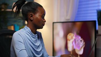 Stressed busy african woman with headache working from home late at night on laptop. Tired focused employee using modern technology network wireless doing overtime for job reading writing, searching photo