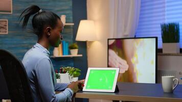 Focused black manager woman looking at tablet with green screen, studying from home using internet technology sitting in living room working overtime. Using mockup chroma key display computer. photo