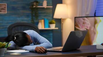 Exhausted overload black businesswoman falling asleep on desk with open laptop monitor while working from home. Busy employee using modern technology network wireless doing overtime sleeping on table. photo