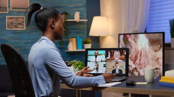 Black businesswoman on conference working remotely from home sitting at desk late at night. Lady using modern technology network wireless talking on virtual meeting at midnight doing overtime photo