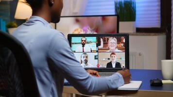 African freelancer working remotely discussing with partners online using laptop sitting in Livin room. Using modern technology network wireless talking on virtual meeting at midnight doing overtime photo