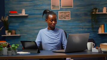 African woman using laptop and tablet in same time in office living room working overtime. Busy focused black employee using modern technology network wireless overworking writing, searching. photo