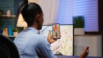 Black young lady discussing on webcam with family using smartphone taking a break after working overtime at home. Freelancer working in personal workplace having meeting. photo