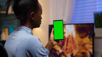 Lady looking at green screen smartphone while relaxing at home sitting on sofa. Woman holding a mobile phone with mockup template chroma key isolated cell phone display using techology internet photo