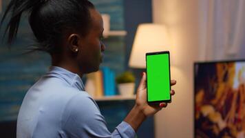 Housewife holding smartphone with chroma screen on hand looking at mockup. Reading on green screen template chroma key isolated mobile phone display using techology internet sitting on cozy couch photo