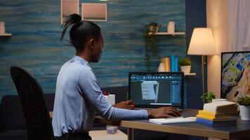 African lady enginer analysing digital mechanism of container checking prototype of project looking on laptop sitting at desk in living room office late night. Black employee using modern technology photo