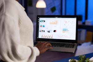 Close up of dark skin business woman typing on laptop standing in start up business late at night. Busy focused employee using modern technology network wireless overtime. photo