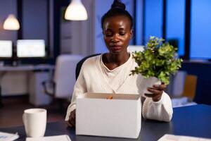 Depressed african woman after being dismissed from work late at night. Unemployed packing things late at night. woman leaving workplace office in midnight. photo