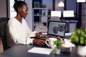African mechanical designer working on computer late at night doing overtime to finish project. Freelancer studying prototype idea on pc showing cad software on device display. photo