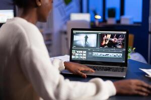 Black editor working overtime at new project editing audio film montage sitting in start-up business office. Woman content creator using professional laptop, modern technology, network wireless photo