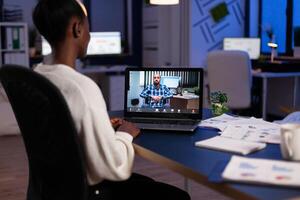 African american businesswoman discussing company strategy with remote collegue during online videocall meeting conference on laptop. Business teleconference call in startup office photo