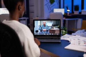 African american businesswoman discussing company strategy with remote collegue during online videocall meeting conference on laptop. Business teleconference call in startup office photo